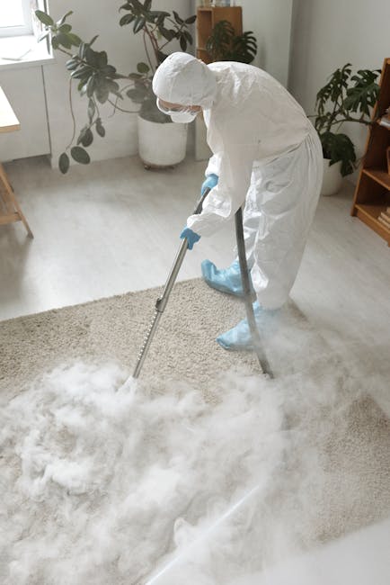 A person using a yellow vacuum cleaner with a black hose attachment to clean a patterned beige and green carpet in a residential living room. The individual is wearing light-colored sneakers and jeans, and is operating the vacuum head over the carpet's surface, which appears dust-free and well-maintained. The room is illuminated with natural or ambient light, highlighting the detailed floral design on the carpet. The setting suggests a thorough domestic cleaning process with attention to surface hygiene. Carpet Cleaners Lambeth specializes in high-quality cleaning services, including deep carpet cleaning and sanitisation, ensuring a fresh and hygienic environment.