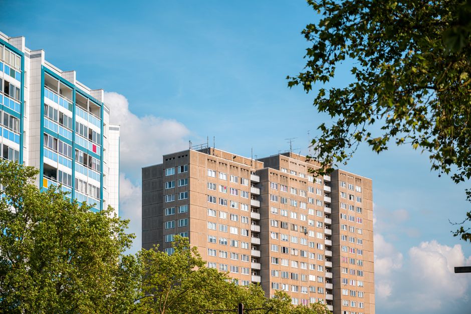 A daytime exterior view of tall residential apartment buildings, with the building on the left featuring a modern design with glass balconies and white framing, while the central building has a tradit